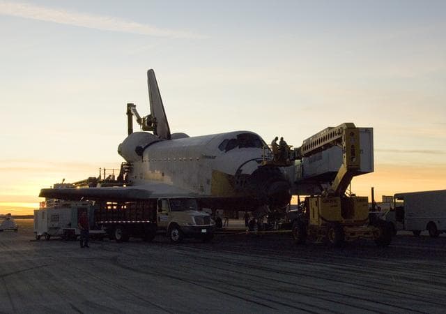 NASA image: As the sun sets over the high desert, NASA technicians on mobile high-lifts prepare the shuttle Endeavour for towing off the Edwards Air Force Base runway