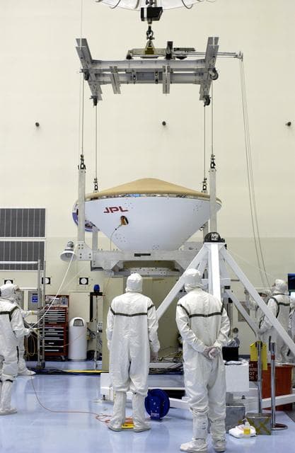 NASA image: KENNEDY SPACE CENTER, FLA. - An overhead crane lifts the Mars Exploration Rover 2 (MER-2) entry vehicle from its stand to move it to a spin table for a dry-spin test.  The MER Mission consists of two identical rovers designed to cover roughly 110 yards each Martian day over various terrain. Each rover will carry five scientific instruments that will allow it to search for evidence of liquid water that may have been present in the planet's past.  Identical to each other, the rovers will land at different regions of Mars.  Launch for MER-2 (MER-A) is scheduled for June 5.
