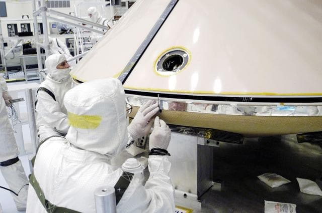 NASA image: KENNEDY SPACE CENTER, FLA. - In the Payload Hazardous Servicing Facility, workers check the attachment between the backshell (above) and heat shield (below) surrounding the Mars Exploration Rover 1 (MER-1).  The aeroshell will protect the rover on its journey to Mars.  NASA's twin Mars Exploration Rovers are designed to study the history of water on Mars. These robotic geologists are equipped with a robotic arm, a drilling tool, three spectrometers, and four pairs of cameras that allow them to have a human-like, 3D view of the terrain. Each rover could travel as far as 100 meters in one day to act as Mars scientists' eyes and hands, exploring an environment where humans can't yet go.  MER-1 is scheduled to launch June 25 as MER-B aboard a Delta II rocket from Cape Canaveral Air Force Station.